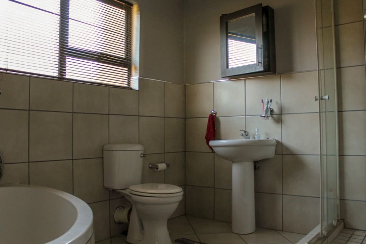 A functional bathroom featuring a pedestal basin, toilet, corner bathtub, and a separate shower enclosure with tiled walls and flooring.