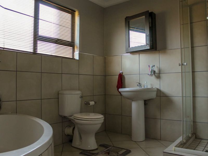 A functional bathroom featuring a pedestal basin, toilet, corner bathtub, and a separate shower enclosure with tiled walls and flooring.
