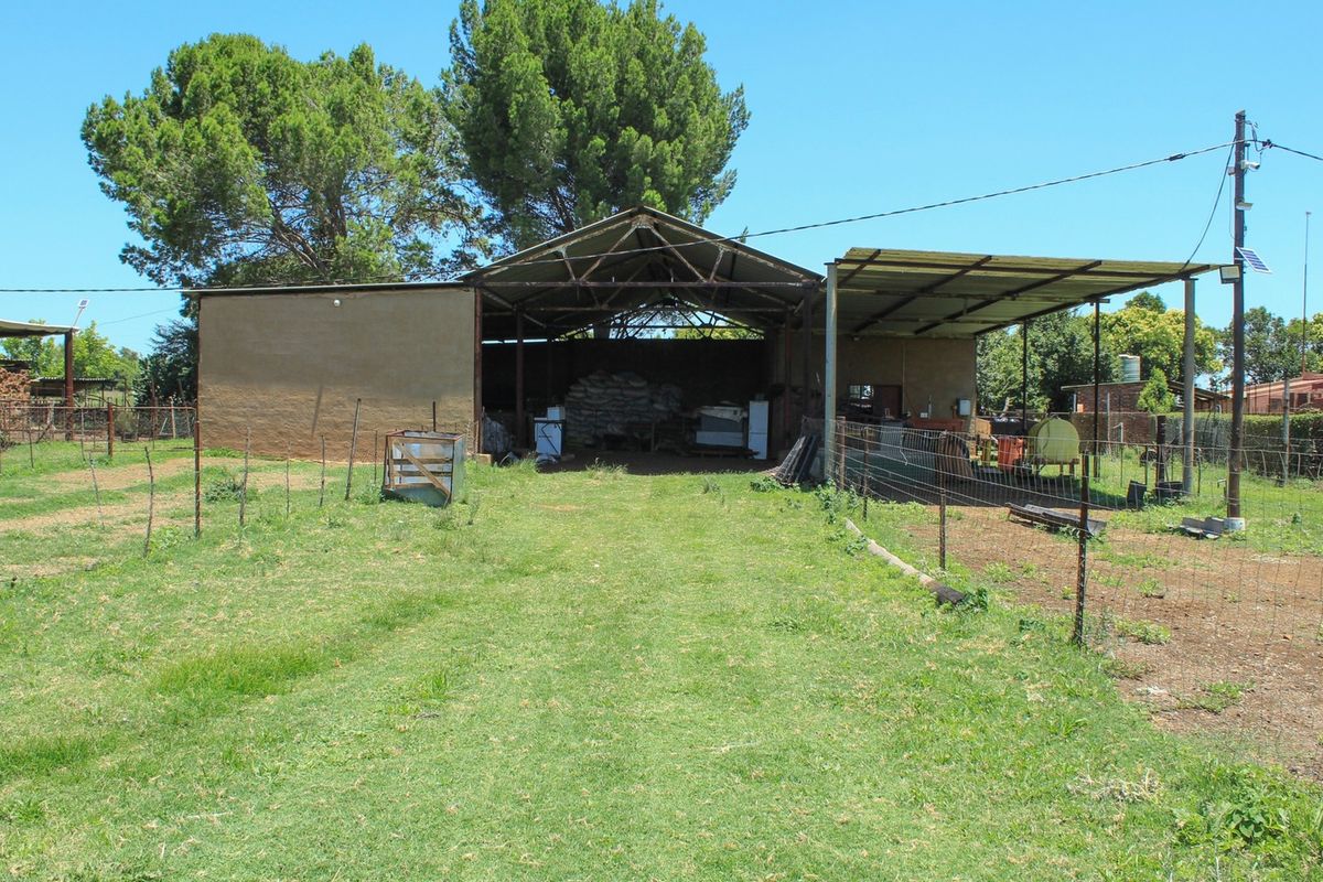 A large agricultural barn or storage shed with an attached open-sided shelter, situated on a grassy farm plot.