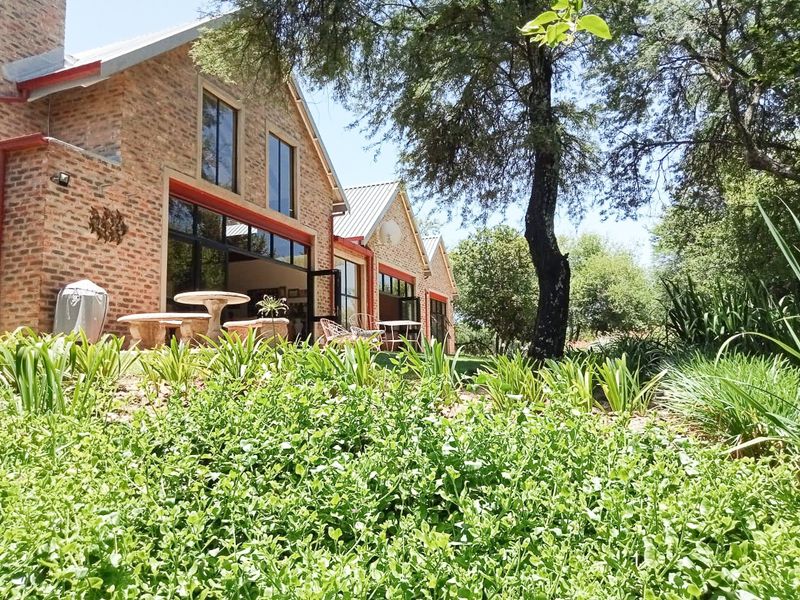 Rear view of a charming exposed brick small holding residence featuring large glass doors opening onto a lush, well-maintained garden.