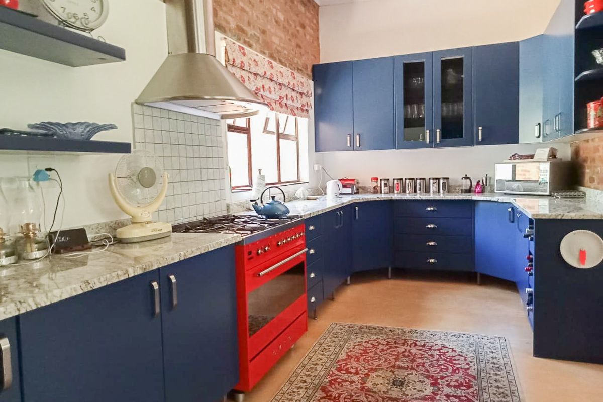 A vibrant kitchen featuring blue cabinetry, granite countertops, a striking red gas stove, and an exposed brick wall, offering a unique and functional cooking space.