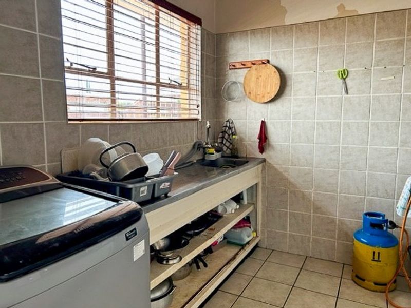 A functional laundry area featuring tiled walls, a stainless steel sink, and tiled flooring, providing a practical space for utility tasks.
