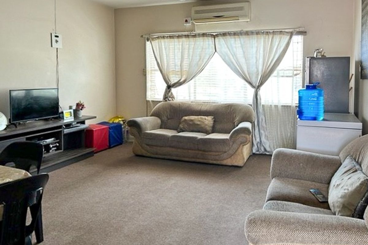 A spacious living room featuring wall-to-wall carpeting, a ceiling fan, and a wall-mounted air conditioning unit, providing a functional and comfortable living space.