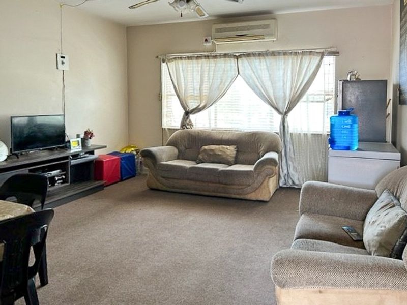 A spacious living room featuring wall-to-wall carpeting, a ceiling fan, and a wall-mounted air conditioning unit, providing a functional and comfortable living space.