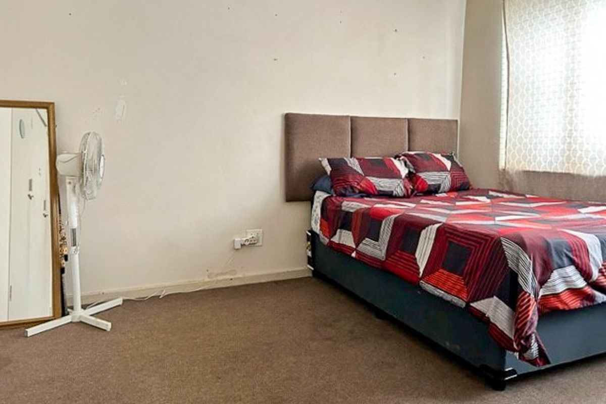 A bedroom featuring carpeted flooring and a wall-mounted headboard, requiring cosmetic updates to the wall finishes and flooring.
