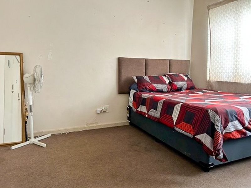 A bedroom featuring carpeted flooring and a wall-mounted headboard, requiring cosmetic updates to the wall finishes and flooring.