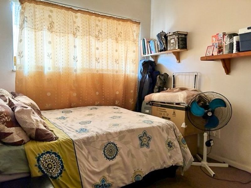 A functional bedroom featuring a window with curtain treatments and wall-mounted shelving units.