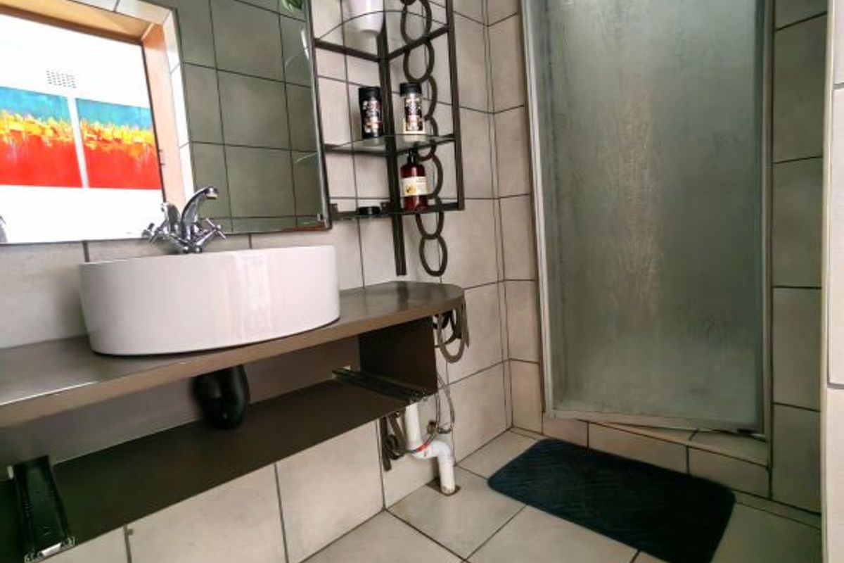 A bathroom featuring a vessel sink on a floating vanity, tiled walls and flooring, and a glass-enclosed shower stall.