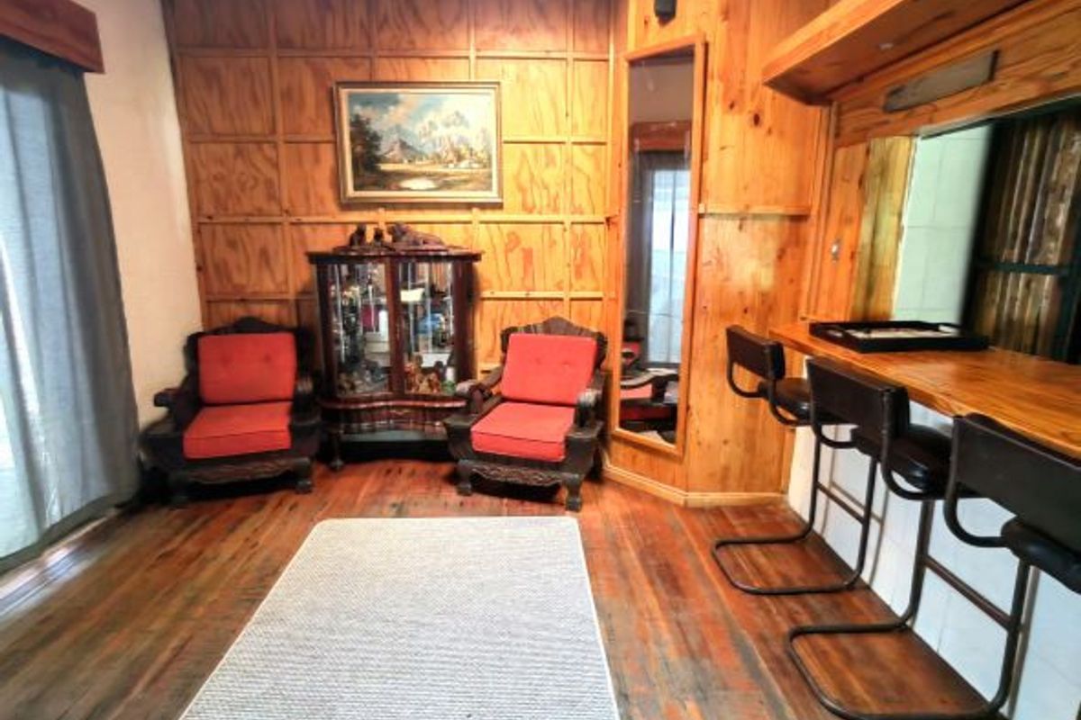 A rustic living area featuring extensive wood paneling, timber flooring, a built-in bar counter with stools, and a mirrored corner feature.