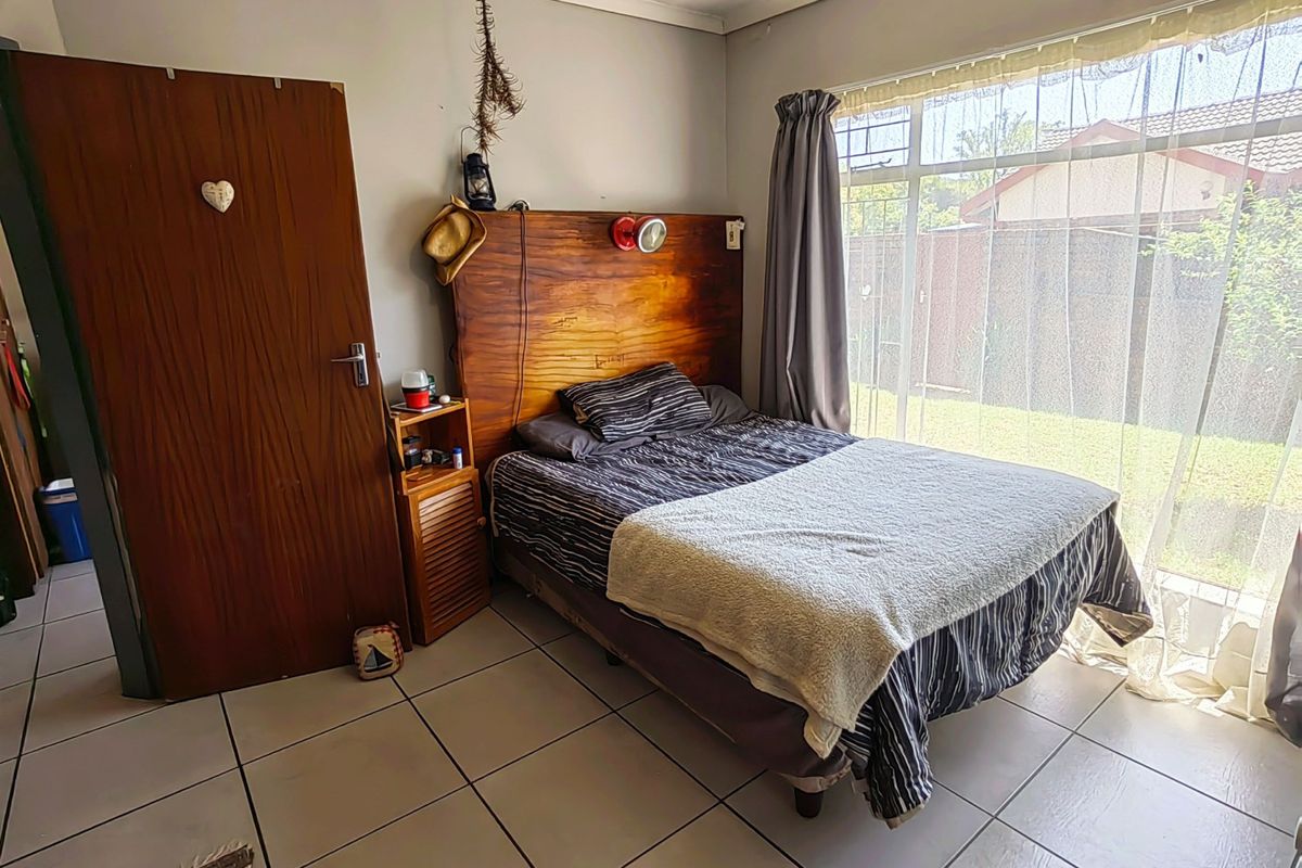 A bedroom featuring large floor tiles, a built-in wooden headboard, and a sliding glass door providing access to the garden area.