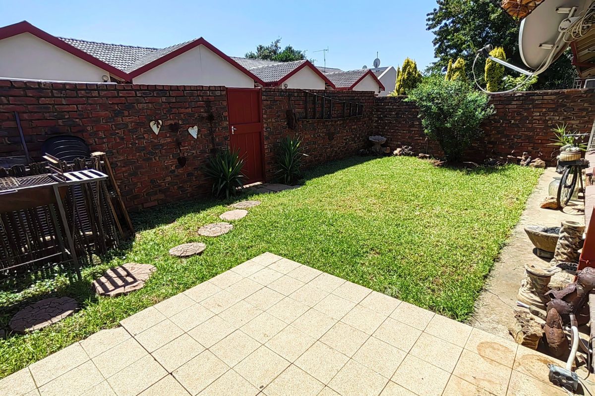 A private rear garden featuring a paved patio area, a well-maintained lawn, and secure perimeter brick walling with a side access gate.