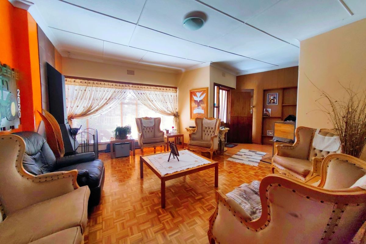 A spacious living room featuring traditional parquet flooring, a built-in fireplace, and large windows that provide ample natural light.