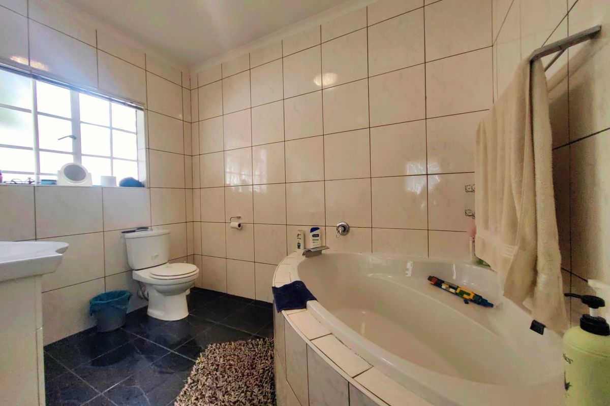 A functional bathroom featuring a built-in corner bathtub, a pedestal basin, and a toilet, finished with floor-to-ceiling wall tiles.