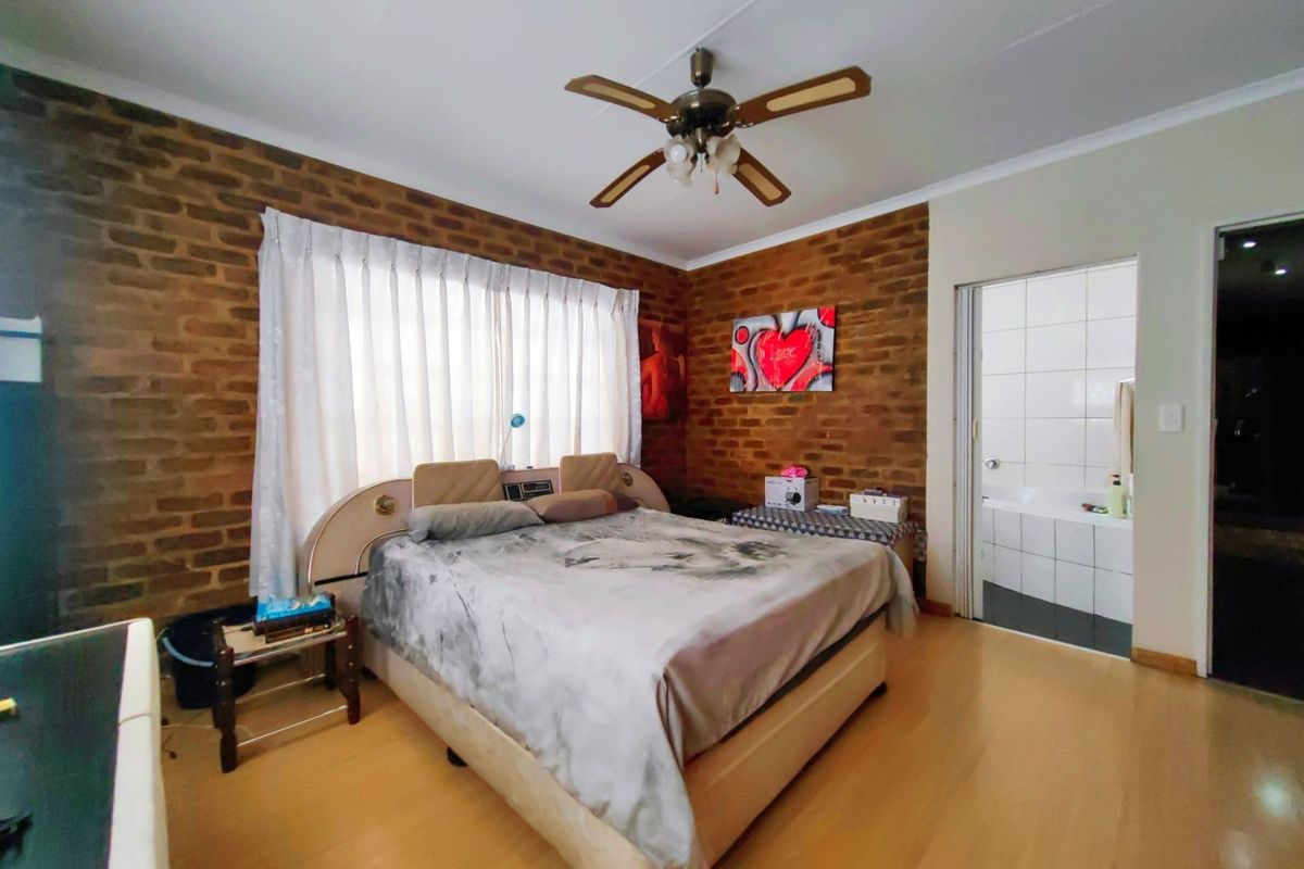 Spacious bedroom featuring an exposed brick feature wall, laminate flooring, and an en-suite bathroom access.