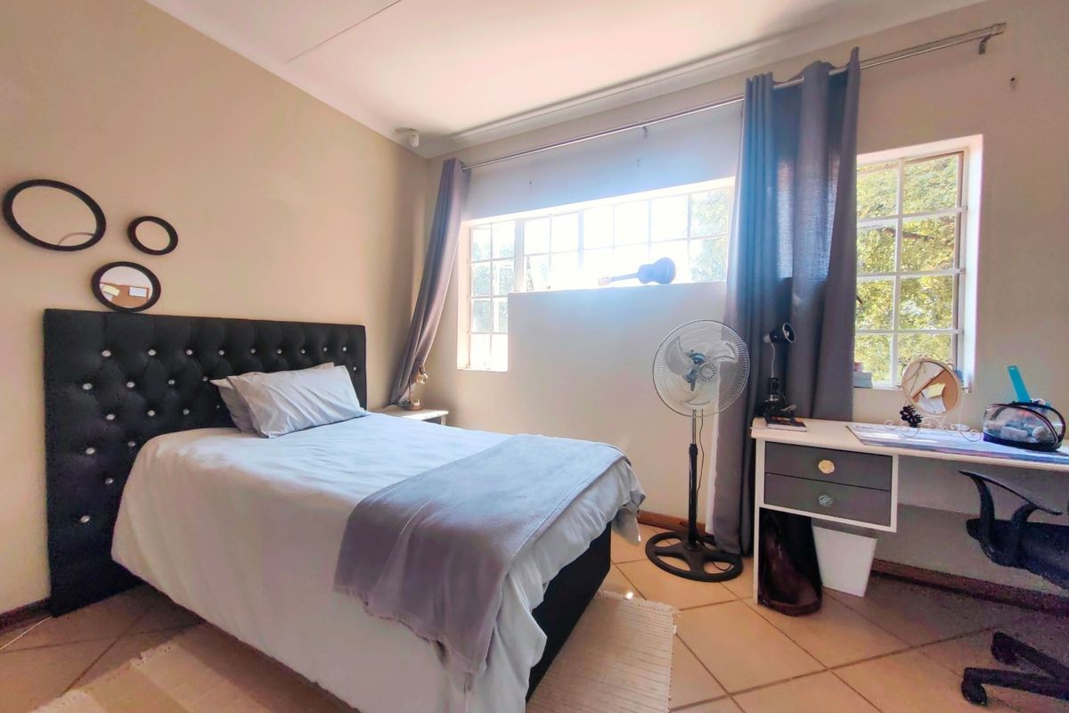 A well-lit bedroom featuring tiled flooring, large windows with curtain tracks, and neutral wall tones, providing a functional and comfortable living space.