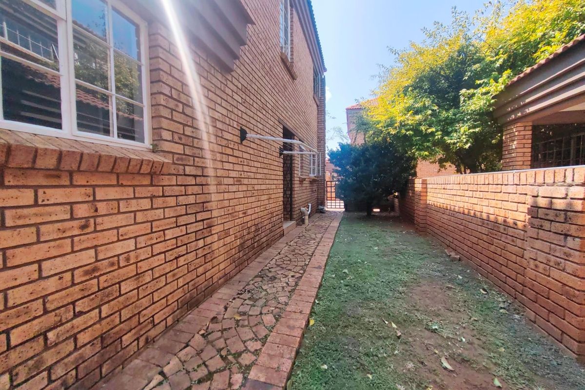 A side exterior view of the townhouse featuring a brick facade, paved walkway, and a small private garden area.
