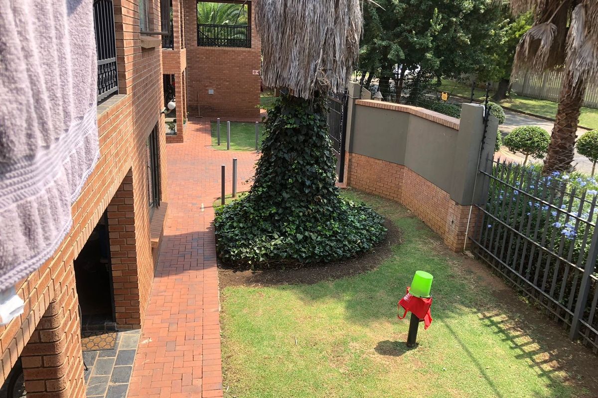 A view of the apartment complex exterior featuring a brick-paved walkway, a small lawn area, and perimeter boundary walls with metal fencing.