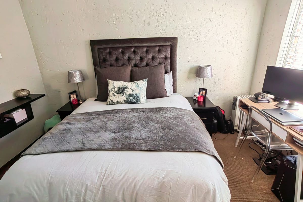 A functional bedroom featuring a built-in wall shelf and carpeted flooring, providing a comfortable space with natural light from the window.