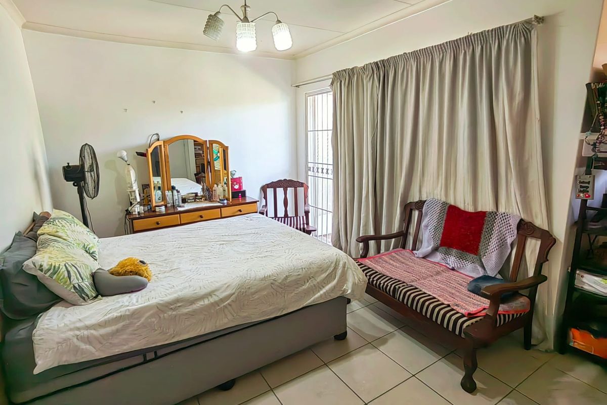 A spacious bedroom featuring tiled flooring, a ceiling light fixture, and a sliding door with security gate providing access to the exterior.