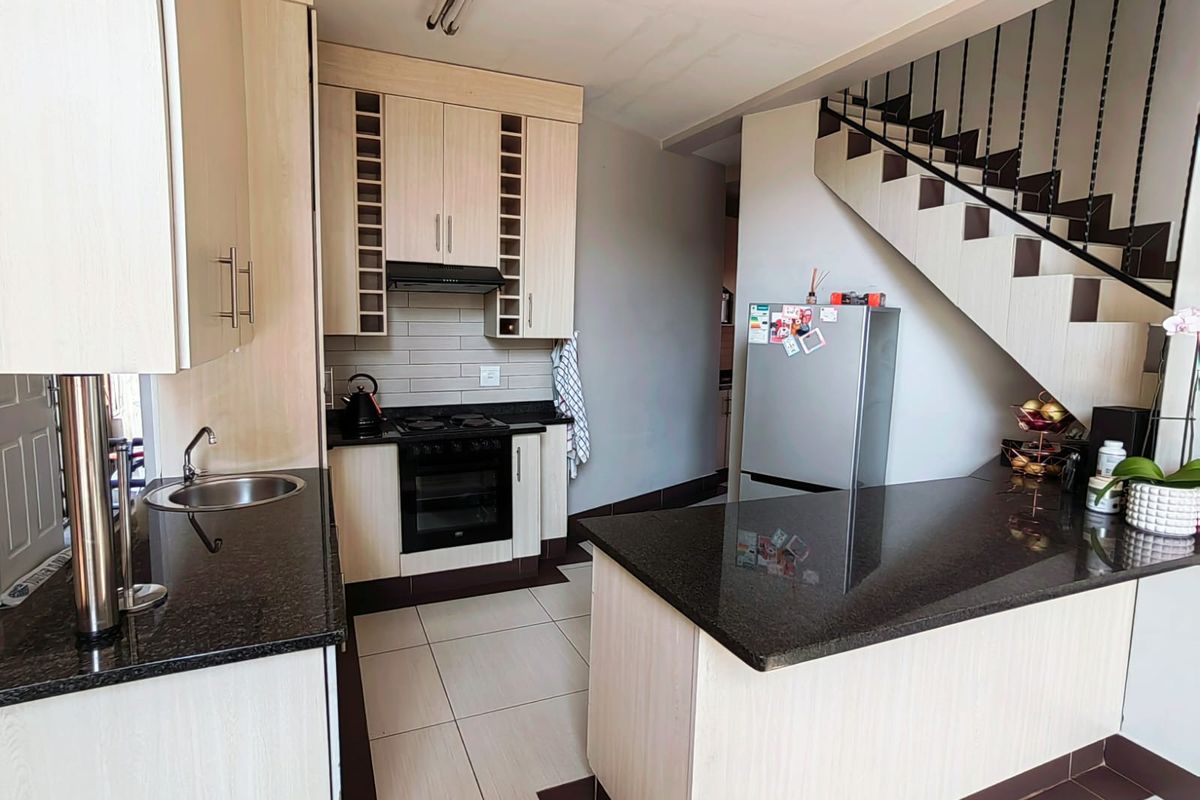 A functional kitchen featuring light wood cabinetry, dark granite countertops, built-in oven, hob, and extractor fan, with an integrated breakfast bar and staircase access.