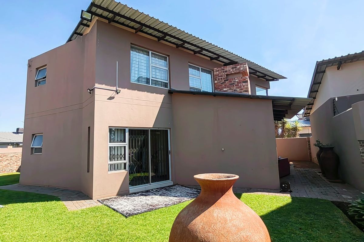 Rear view of the townhouse featuring a paved patio area, small garden, sliding glass doors, and a brick chimney stack.