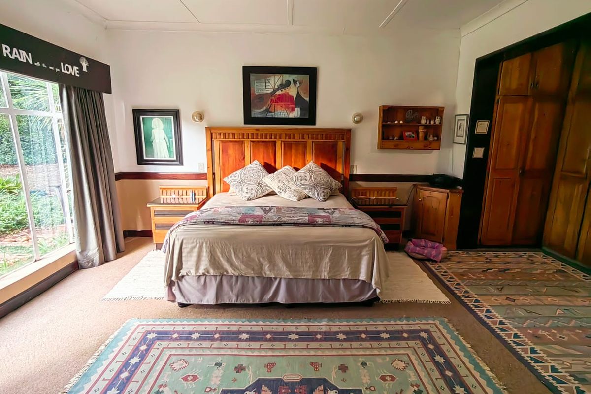 A spacious bedroom featuring large windows with garden views, built-in wooden cabinetry, and neutral wall finishes.