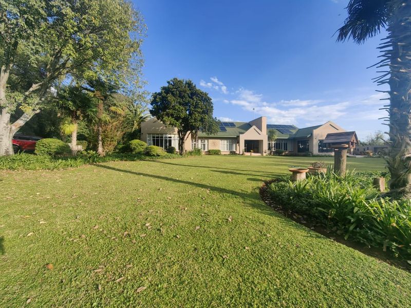 A spacious rear garden view of the property featuring a well-maintained lawn, mature trees, and solar panels installed on the pitched roof.