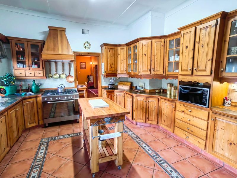Spacious kitchen featuring extensive solid wood cabinetry, a gas stove with extractor hood, built-in microwave, and decorative tiled flooring.