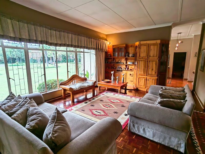 Spacious living room featuring classic parquet flooring, extensive built-in wooden cabinetry, and large windows providing ample natural light and garden views.