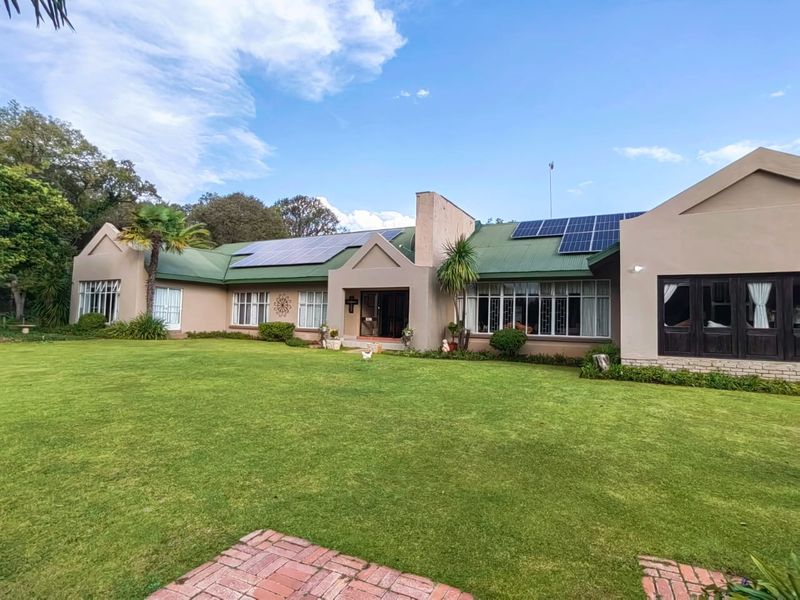 Spacious rear exterior view of the property featuring a large manicured lawn, metal roofing with integrated solar panels, and brick paved pathways.