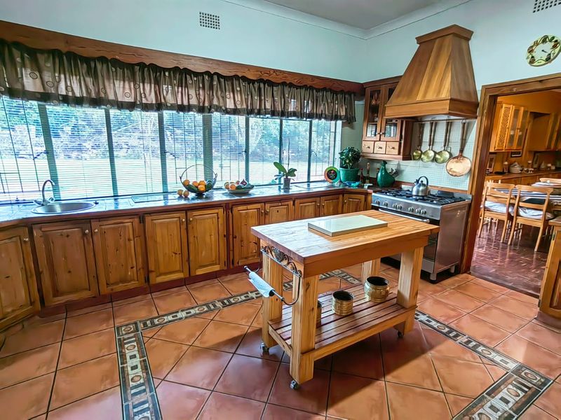 Spacious kitchen featuring traditional wooden cabinetry, tiled flooring with decorative inlay, a gas stove with extractor hood, and large windows overlooking the garden.