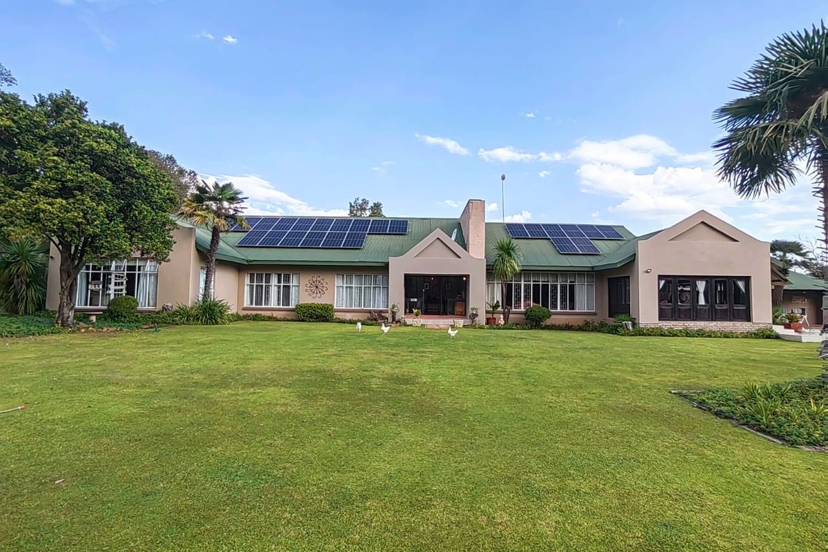 A spacious rear view of the property featuring a well-maintained lawn, large windows, and a roof equipped with solar panels.