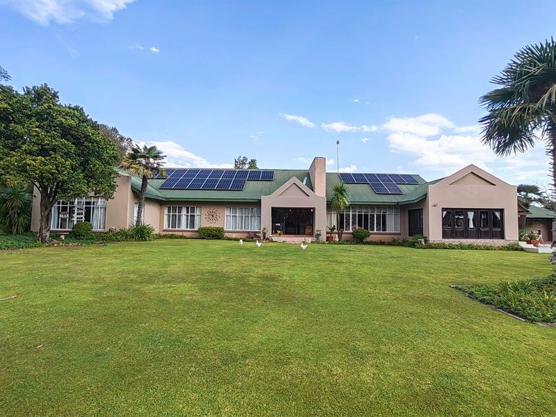 A spacious rear view of the property featuring a well-maintained lawn, large windows, and a roof equipped with solar panels.