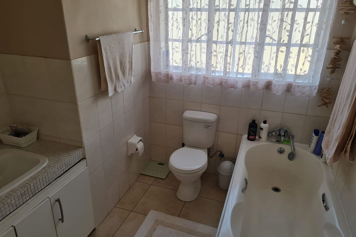 A functional bathroom featuring a built-in vanity with tiled countertop, a standard bathtub with shower mixer, and a toilet.