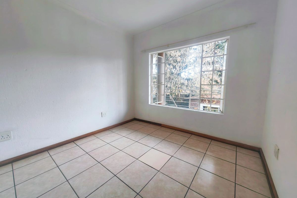 A bright, empty bedroom featuring neutral ceramic floor tiles, a large window with security bars, and clean white walls.