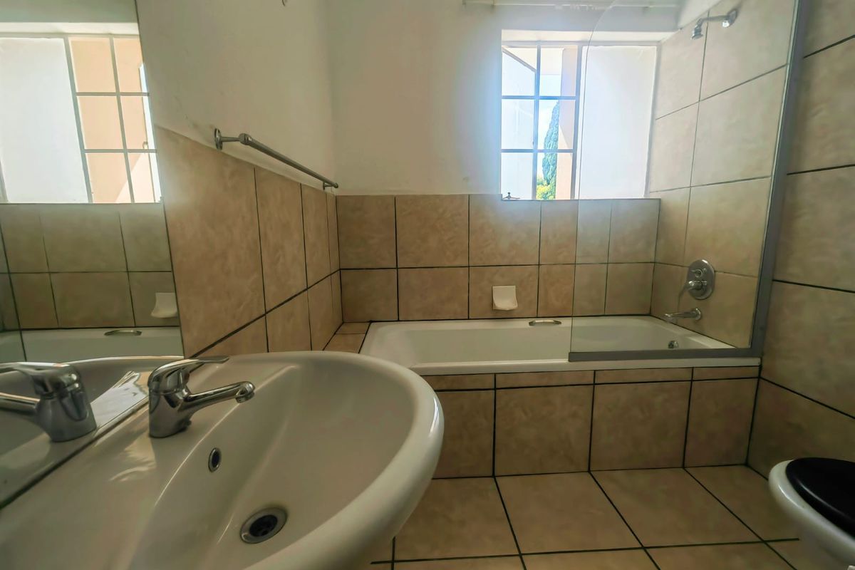A functional bathroom featuring a tiled bathtub with a glass shower screen, a pedestal basin, and a window for natural light.