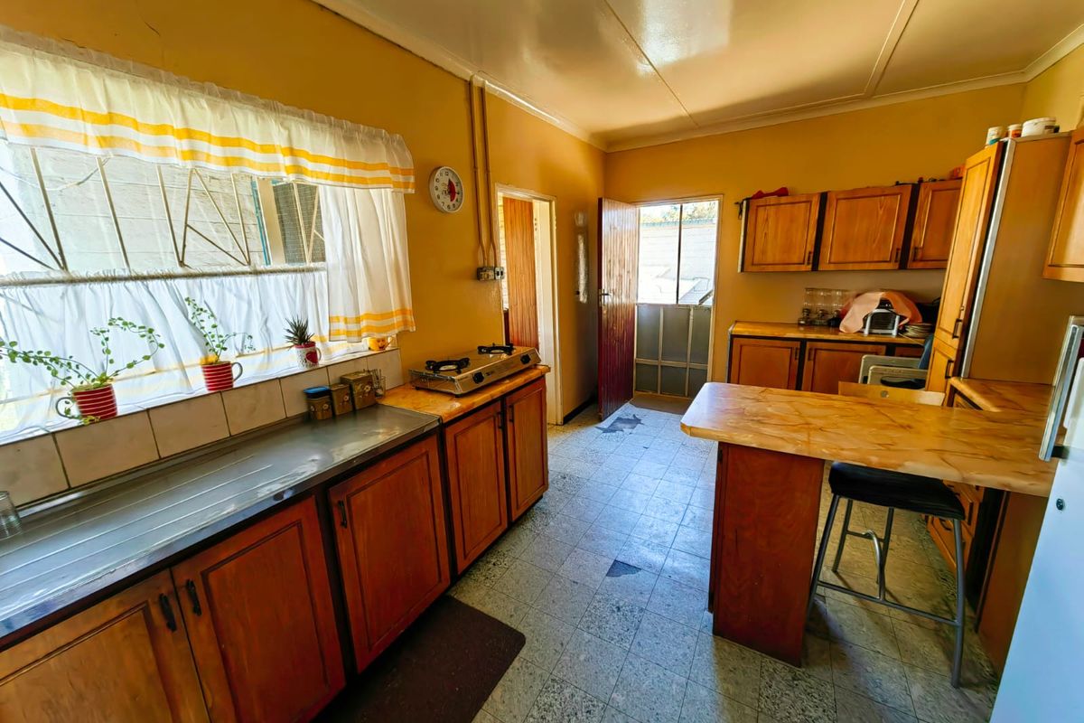 A dated kitchen featuring wooden cabinetry, a stainless steel sink, tiled backsplash, and a breakfast counter, with direct access to an exterior door.