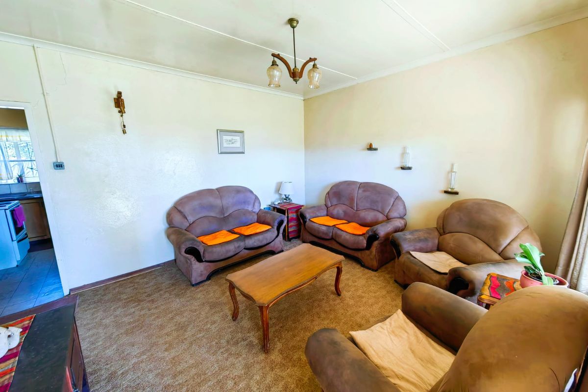 A living room featuring carpet flooring and a central light fixture, showing signs of wear and requiring cosmetic updates.