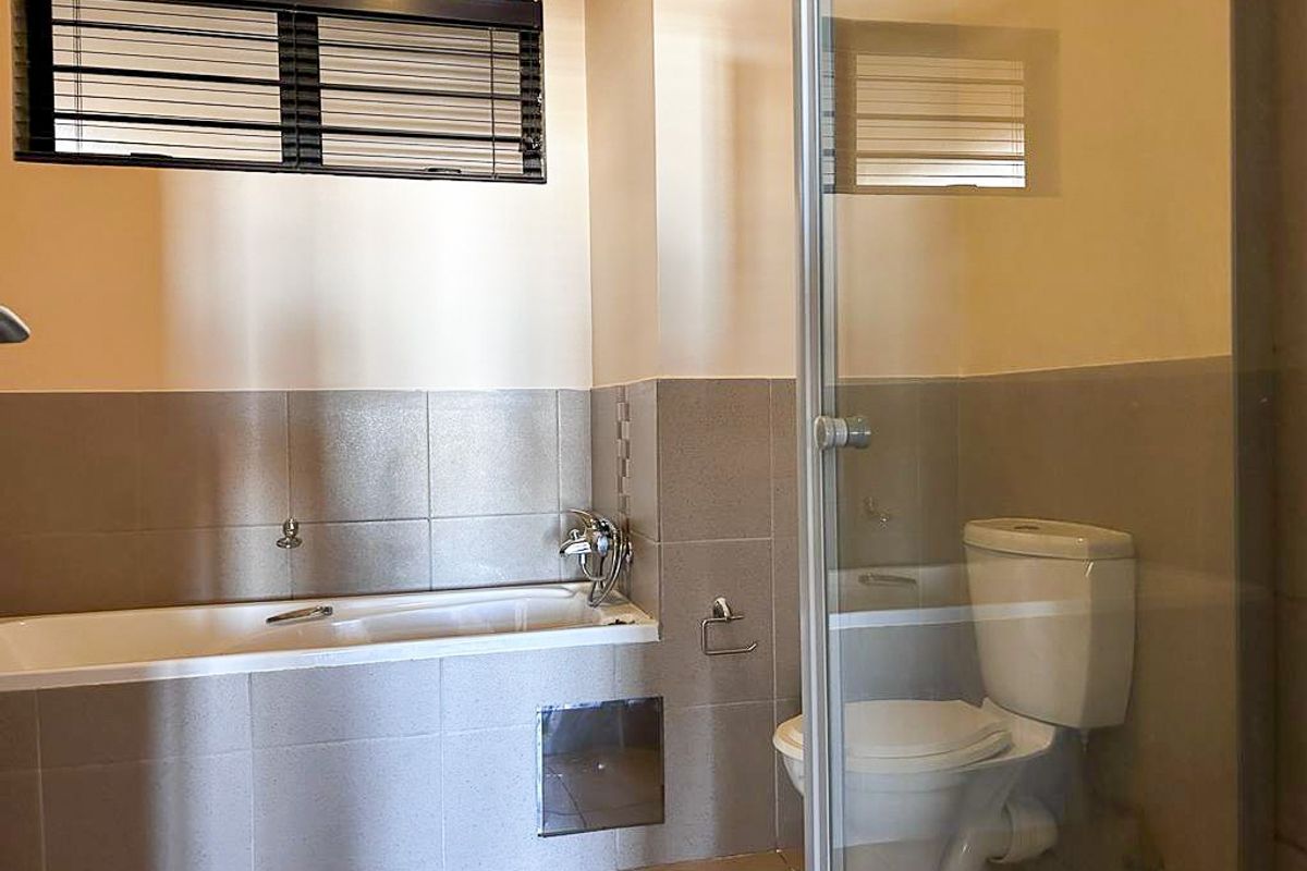 A functional bathroom featuring a built-in bathtub, a separate glass-enclosed shower, and a toilet, finished with neutral wall tiling.