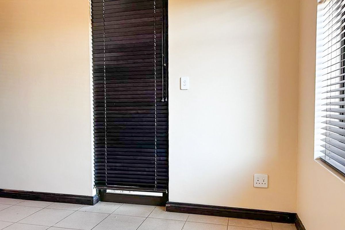 A neutral interior space featuring tiled flooring, dark timber venetian blinds, and standard electrical fixtures.