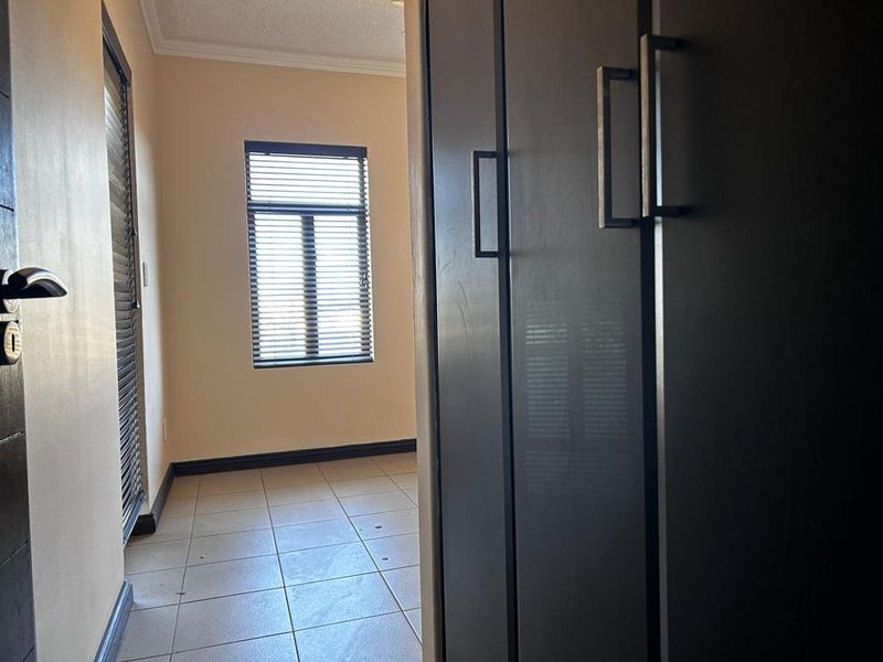 A view from a hallway into a bedroom featuring tiled flooring, built-in dark cabinetry, and a window with fitted blinds.