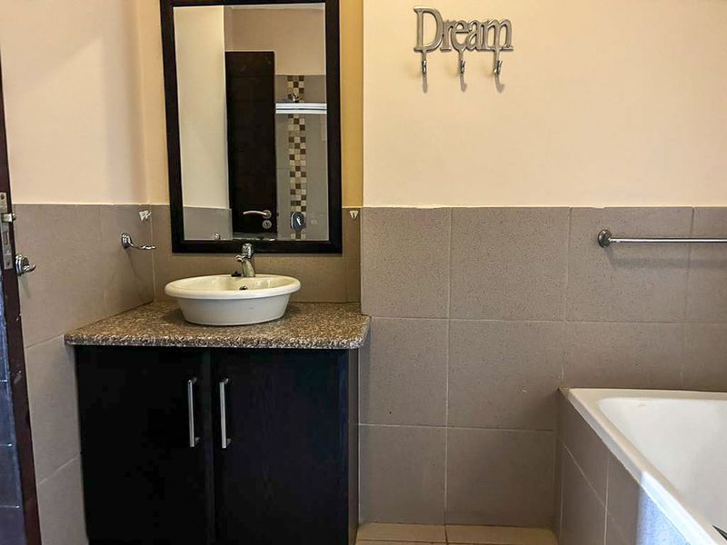 A bathroom featuring a dark vanity cabinet with a granite countertop, vessel sink, framed mirror, and tiled walls with a built-in bathtub.
