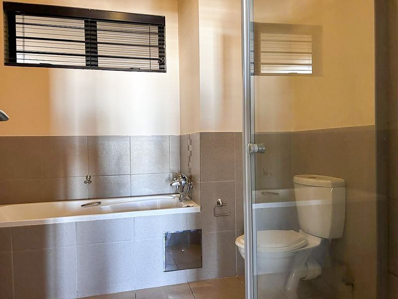 A functional bathroom featuring a built-in bathtub, a separate glass-enclosed shower, and a toilet, finished with neutral wall tiling.