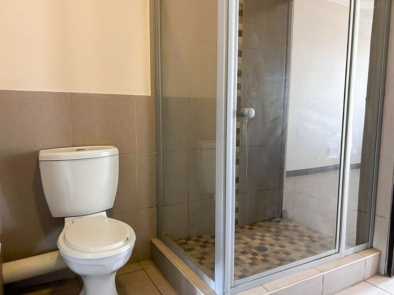 A functional bathroom featuring a glass-enclosed shower and a standard toilet with neutral wall tiling.