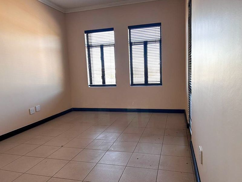 An empty bedroom featuring neutral walls, tiled flooring, and two windows fitted with dark horizontal blinds.