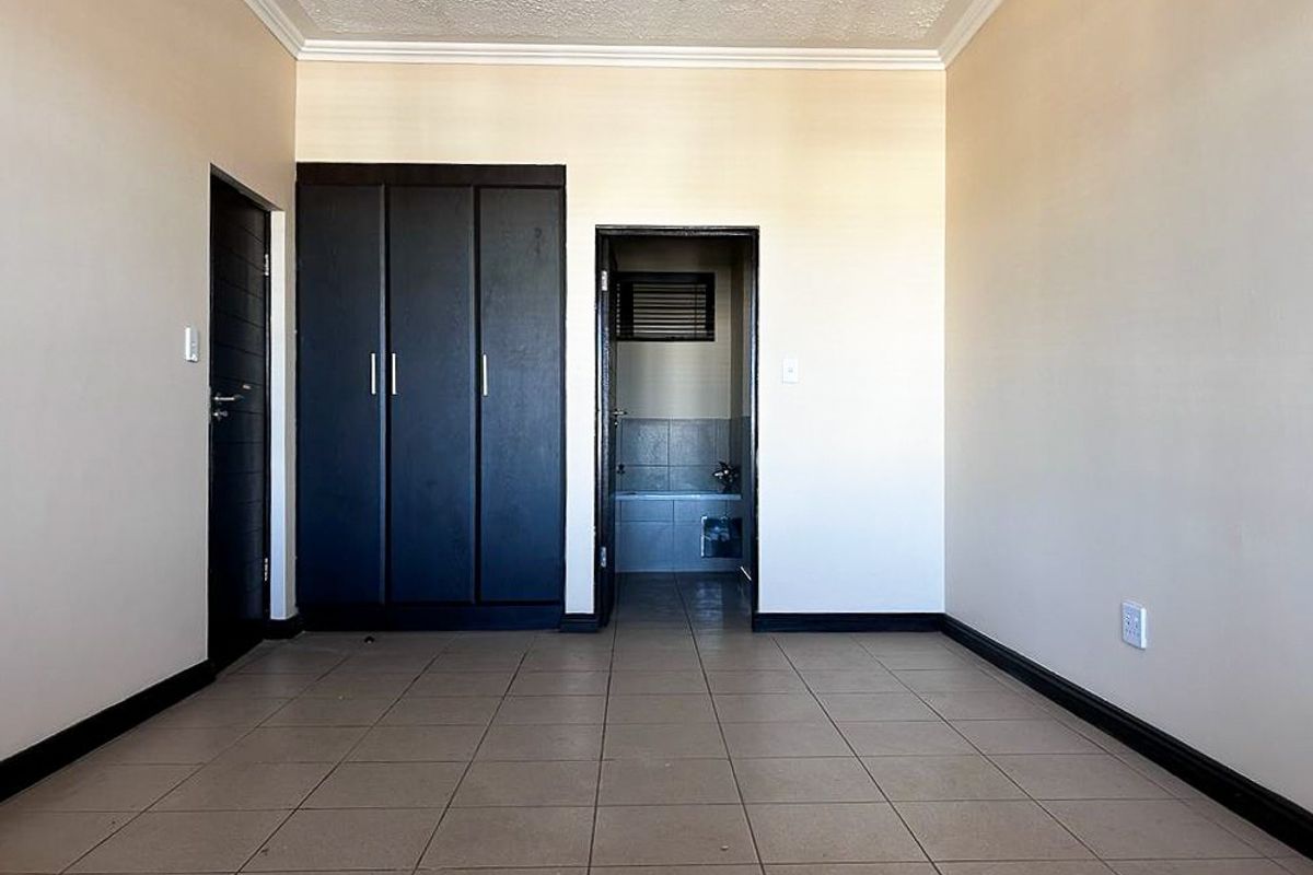 A bedroom featuring tiled flooring, built-in dark cabinetry, and direct access to an en-suite bathroom.