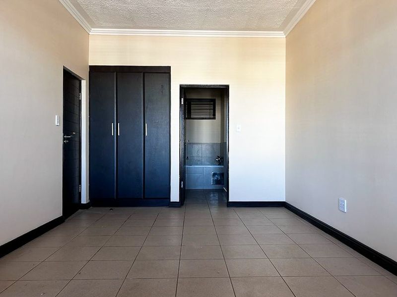 A bedroom featuring tiled flooring, built-in dark cabinetry, and direct access to an en-suite bathroom.