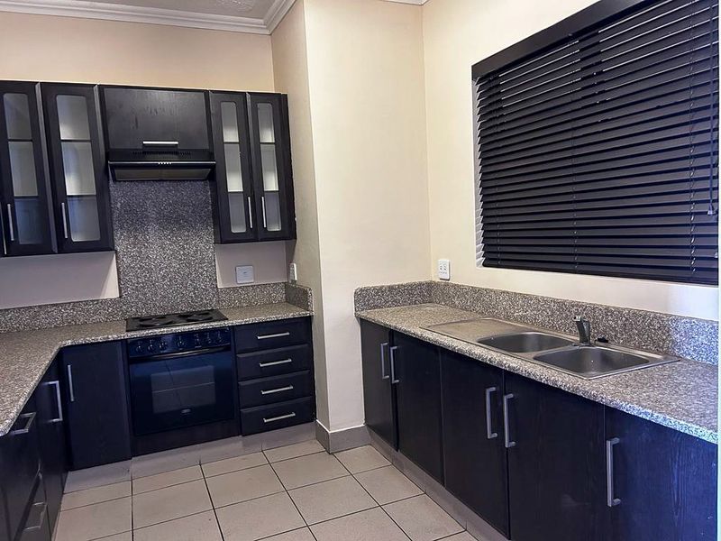 A functional kitchen featuring dark cabinetry, granite countertops, a built-in oven with extractor fan, and a double-basin stainless steel sink.