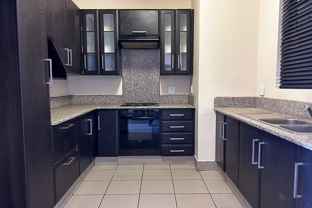 A functional kitchen featuring dark wood cabinetry, granite countertops, a built-in oven, hob, extractor fan, and a double stainless steel sink.