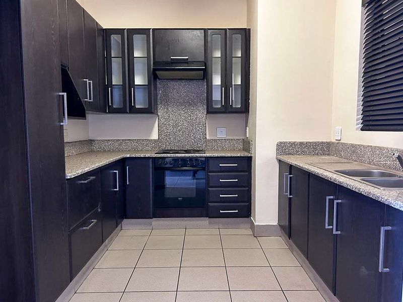 A functional kitchen featuring dark wood cabinetry, granite countertops, a built-in oven, hob, extractor fan, and a double stainless steel sink.